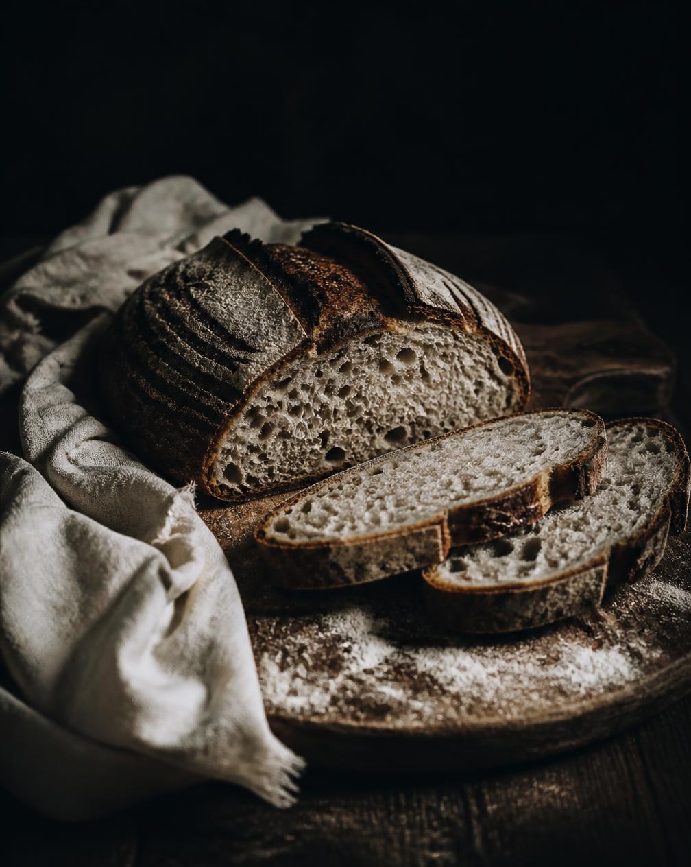 Dark, moody sourdough loaf sliced on a wooden board